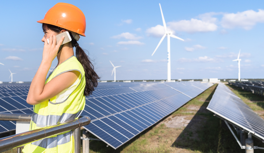 Woman talking on a cell phone near solar panels and wind turbines. 